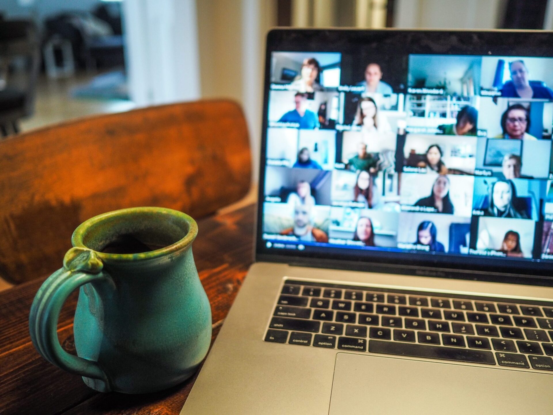 A picture of a laptop on a Zoom call with many participants with a mug next to it.